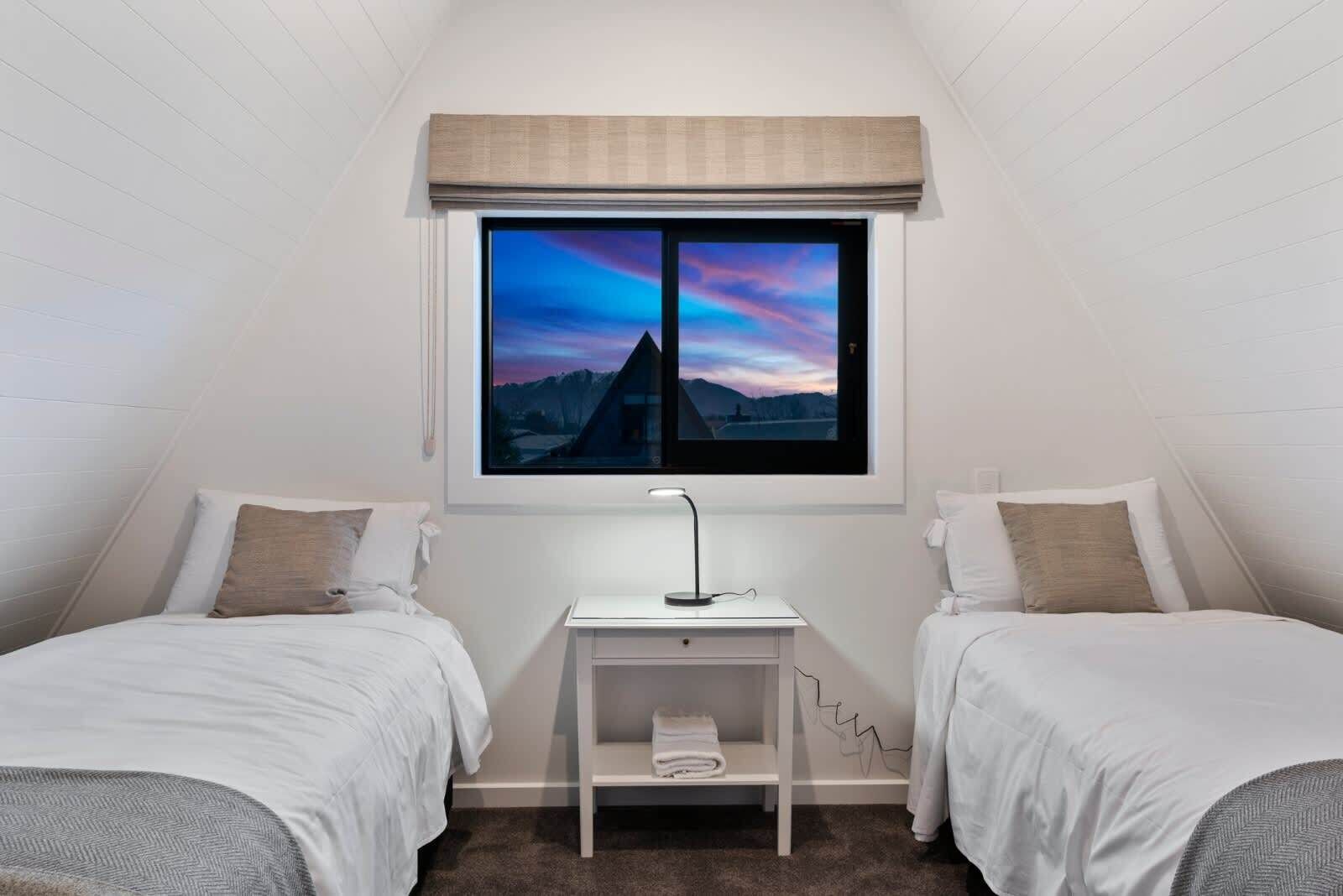 Un dormitorio con dos camas, una mesita de noche y un ventanal con vistas a montañas.
