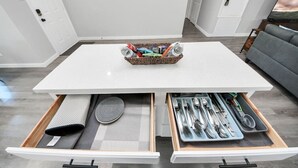 A white table with a basket of snacks and a drawer with cutlery.