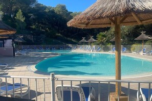Una piscina con agua azul, rodeada de sillas de descanso y sombrillas de paja.