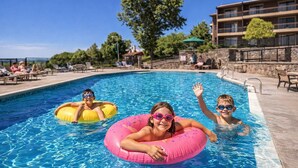Una piscina con gente en círculos inflables, un muro de piedra y un edificio con balcones al fondo.