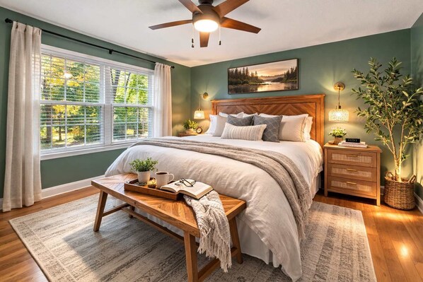 A bedroom with a bed, bedside tables, a nightstand, a window with curtains, a ceiling fan, and a wall-mounted picture.
