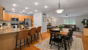 Una cocina moderna con encimeras de granito, electrodomésticos de acero inoxidable y un comedor con mesa y sillas de madera.