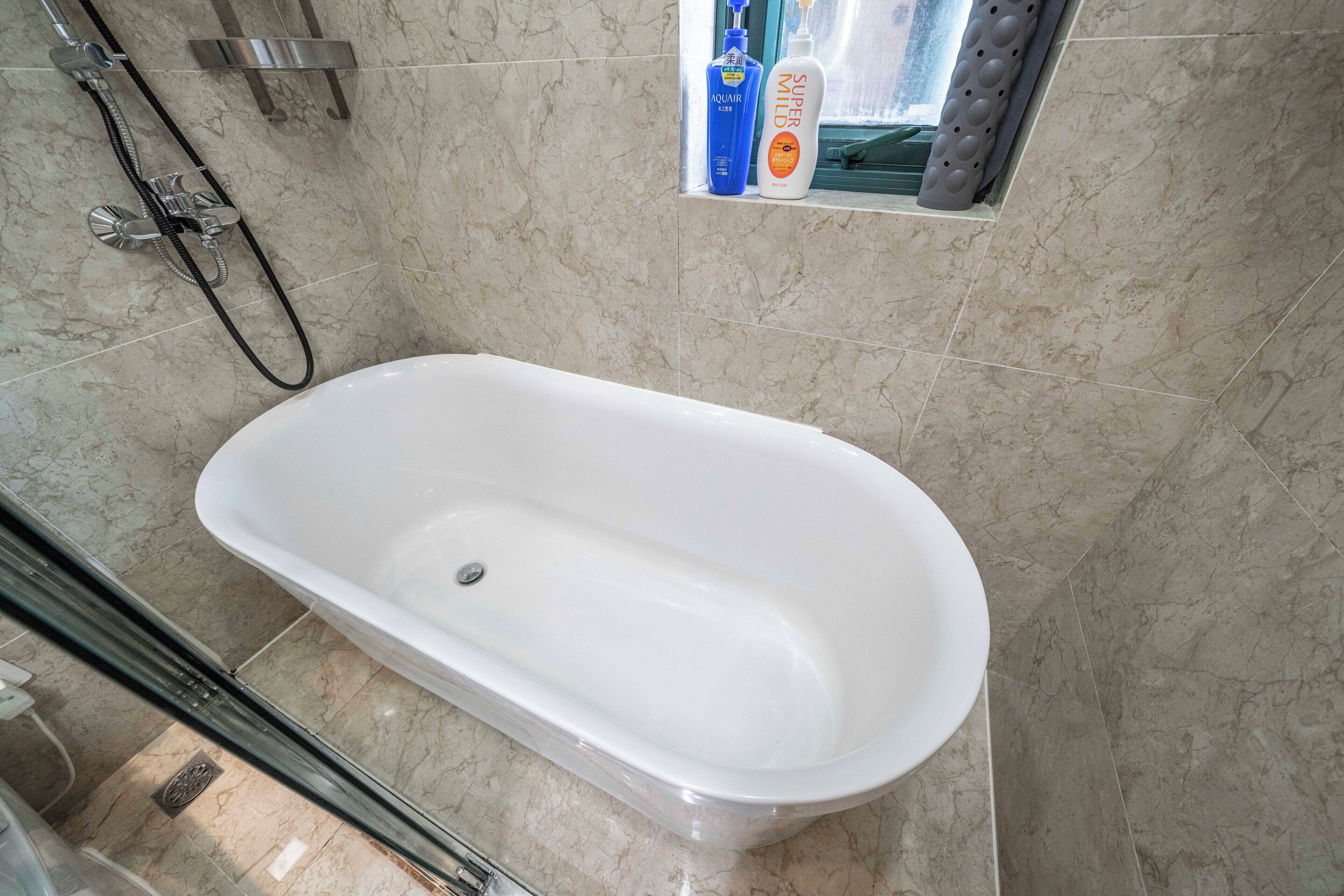 Une salle de bain avec une baignoire blanche, une pomme de douche et des articles de toilette fixés au mur.