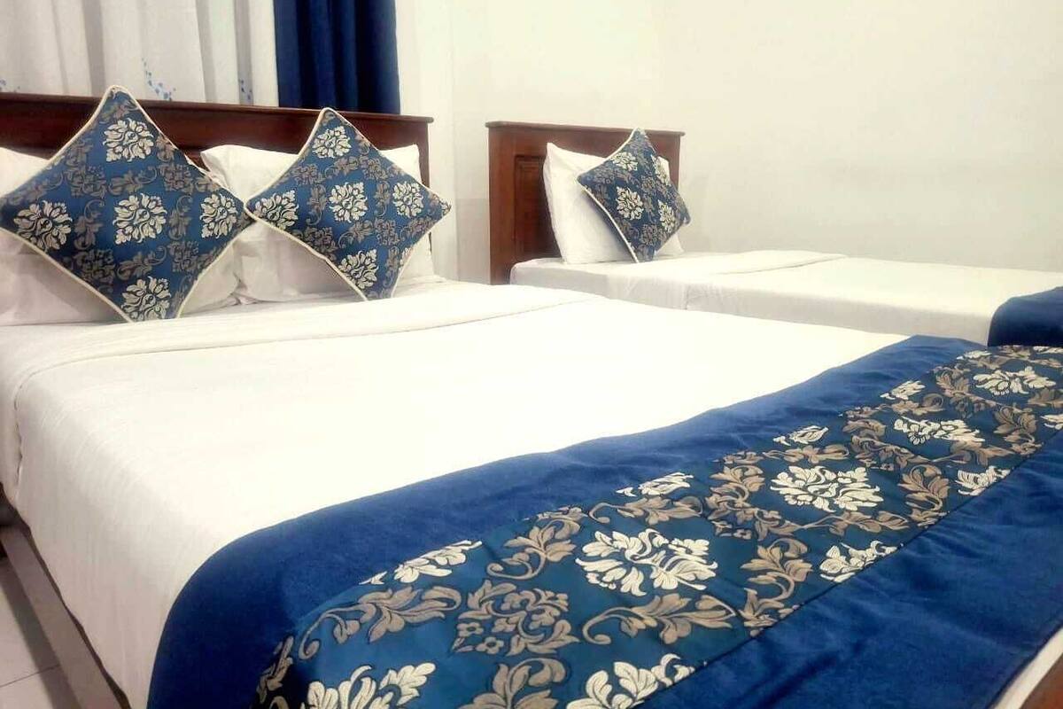 Une chambre d’hôtel avec deux lits, chacun doté d’un matelas blanc et d’une literie à motifs floraux bleus.