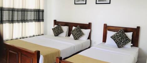 Dos camas de madera con sábanas blancas y almohadas estampadas, una ventana con cortinas a rayas, y dos cuadros en la pared.