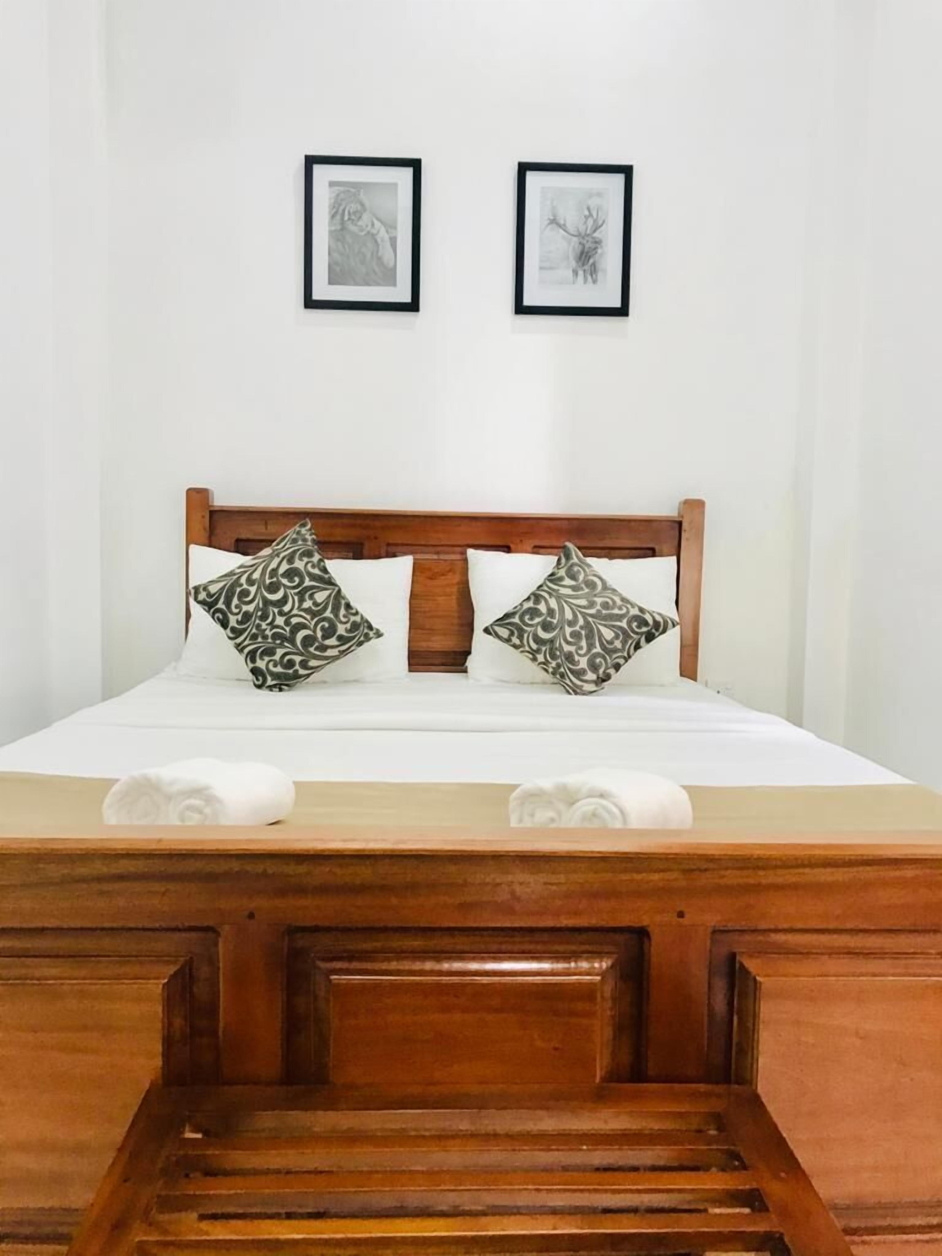 A neatly made bed with two pillows and two towels, a wooden headboard, and two framed pictures on the wall.