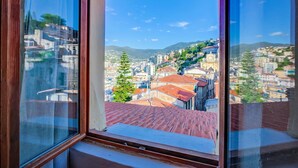 Vista attraverso una finestra con cornice in legno su un paesaggio urbano con edifici, una collina e cielo sereno.