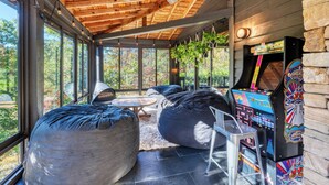 Un espace intérieur accueillant, avec un plafond en bois, de grandes fenêtres et une borne d’arcade rétro.