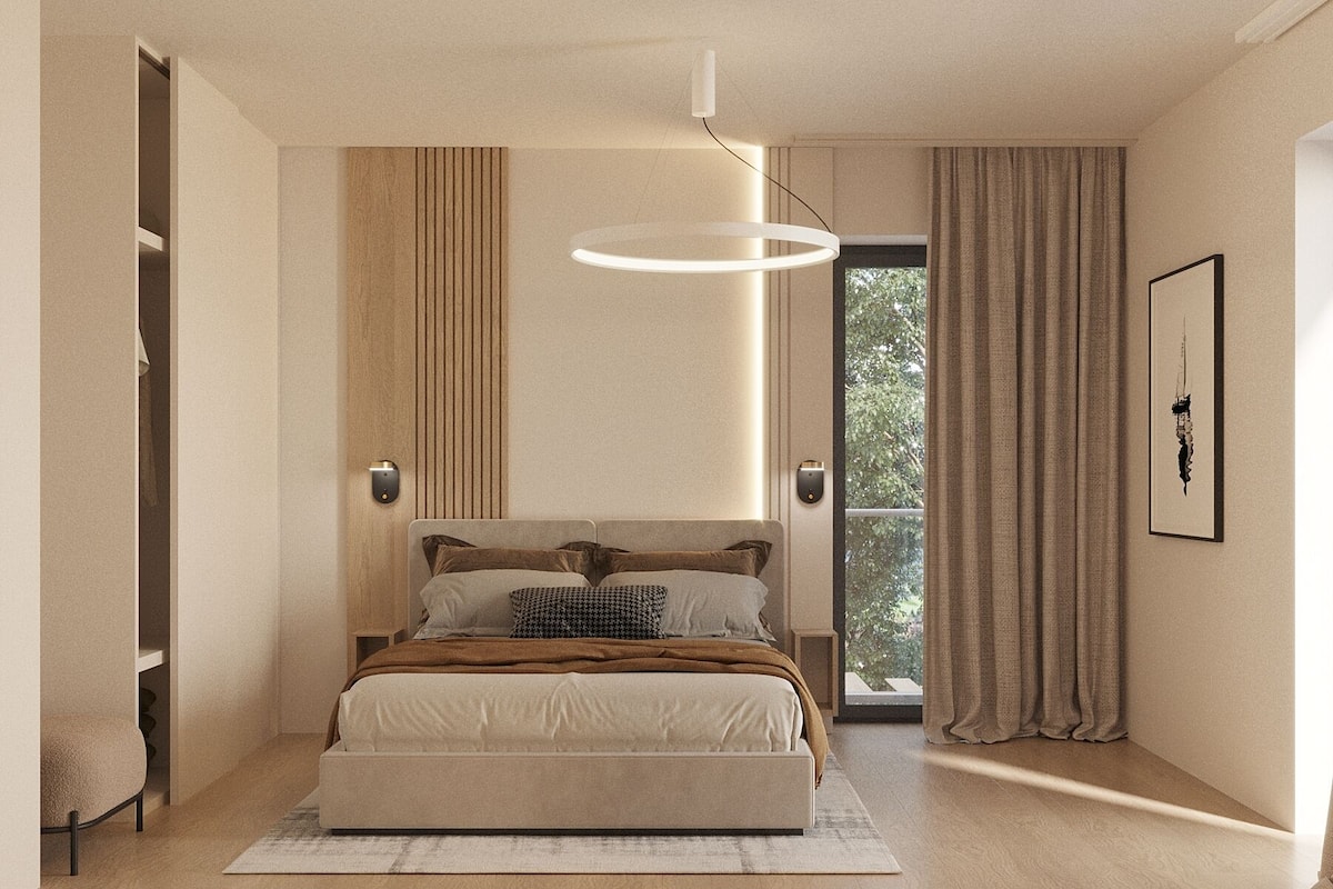 A modern bedroom with a large bed, a hanging light fixture, a view of greenery outside, and a framed artwork on the wall.