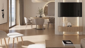 Una sala de estar moderna con un televisor de pantalla plana montado en la pared, un comedor con mesa y sillas, y un amplio ventanal que proporciona luz natural.