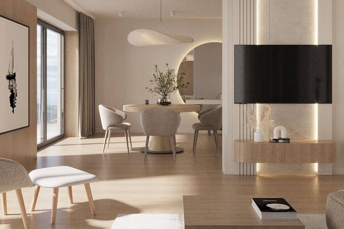 A modern living room with a flat-screen TV mounted on a wall, a dining area with a table and chairs, and a large window providing natural light.