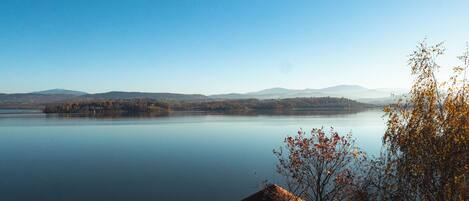 A tranquil lake with a clear sky, surrounded by hills and a small building with a thatched roof in the foreground.