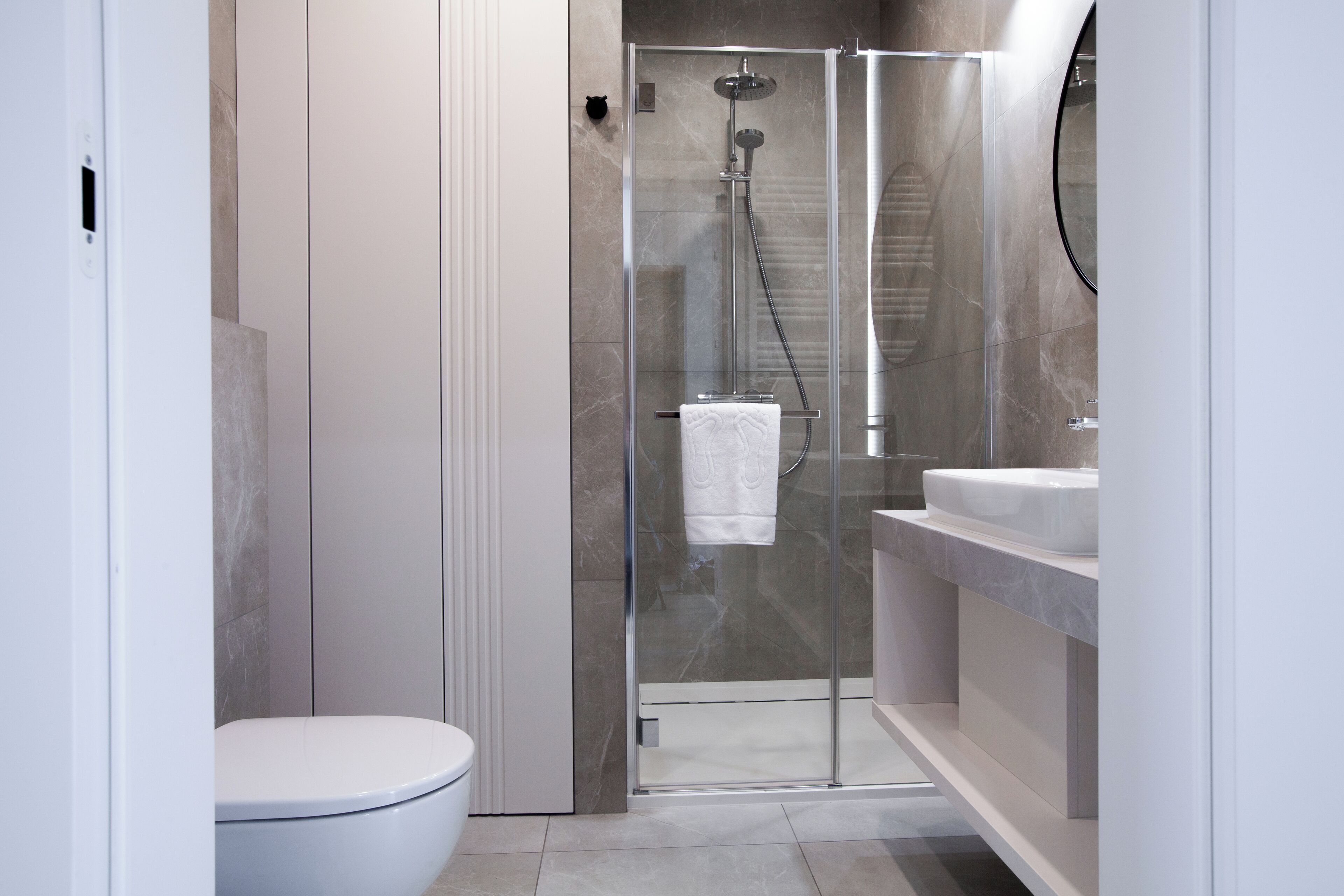 Un baño moderno con ducha envuelta en vidrio, inodoro blanco y zona de lavamanos con azulejos de mármol.