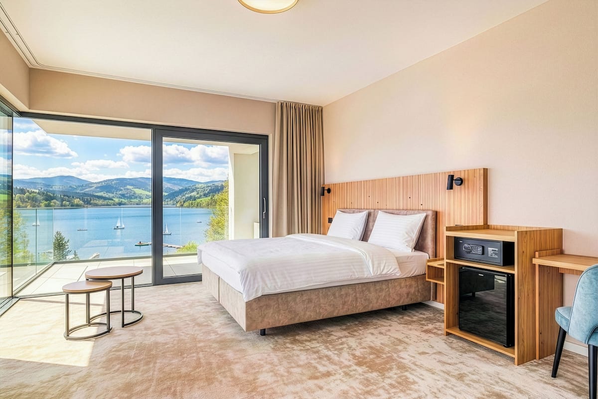 A bedroom with a large window offering a scenic view of a lake and mountains.