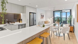 Een moderne keuken met een centraal eiland, een eetgedeelte met een ronde tafel, en uitzicht op de stad door grote ramen.