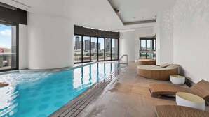 Een binnenzwembad met helder uitzicht op de stadshemel, een zonnedek en een modern interieur.