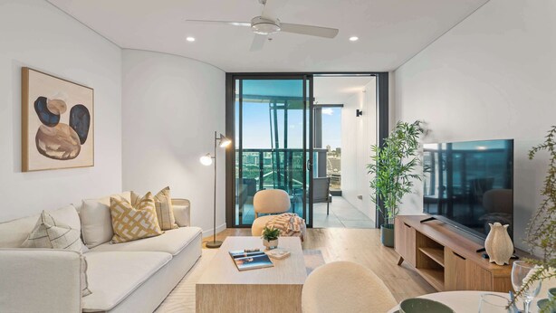 Een moderne woonkamer met een bank, salontafel en televisie. Er is een balkon met uitzicht op de stad.
