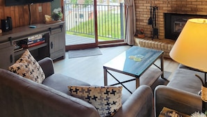 A cozy living room with a TV, sofa, and coffee table, a fireplace, and a balcony with a view. - Cozy CB Condo Close to Ski Resort and Hiking/Biking (Crested Butte)