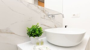 A bathroom with a white marble sink, a small potted plant, and two bottles of liquid soap.