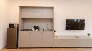 A compact kitchenette with a microwave, refrigerator, and a flat-screen TV mounted on the wall.