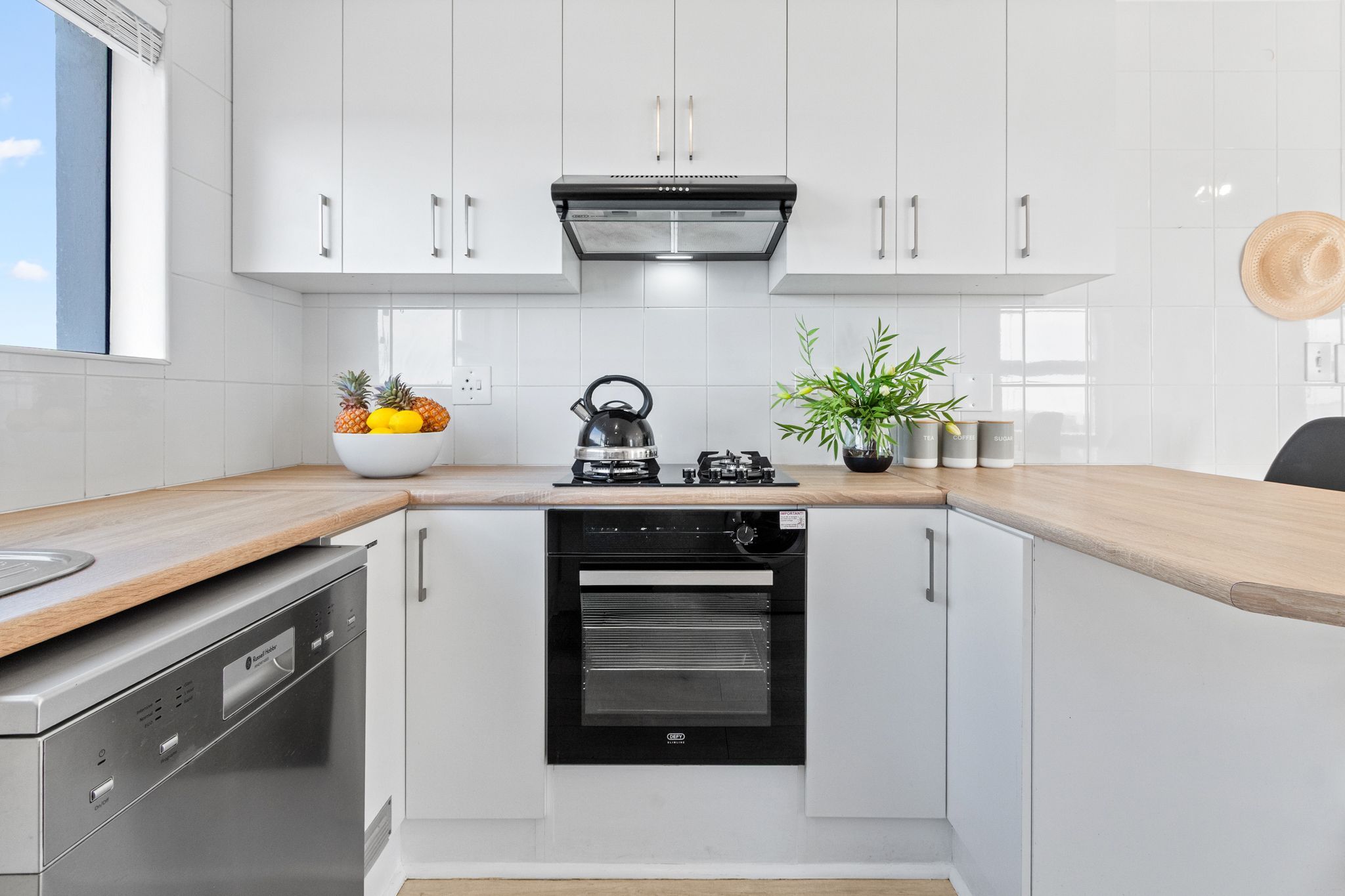 Una cocina moderna con armarios blancos, horno empotrado, lavavajillas y encimera de madera.