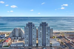 A high-rise building with multiple floors, a parking area, and a view of the ocean.