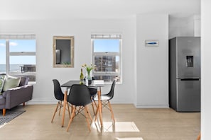 A modern kitchen with a stainless steel refrigerator, a dining table with black chairs, and a view of the city through large windows.