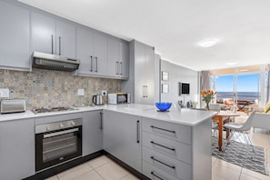 A modern kitchen with grey cabinets, a built-in oven, a microwave, and a large island with a blue bowl.