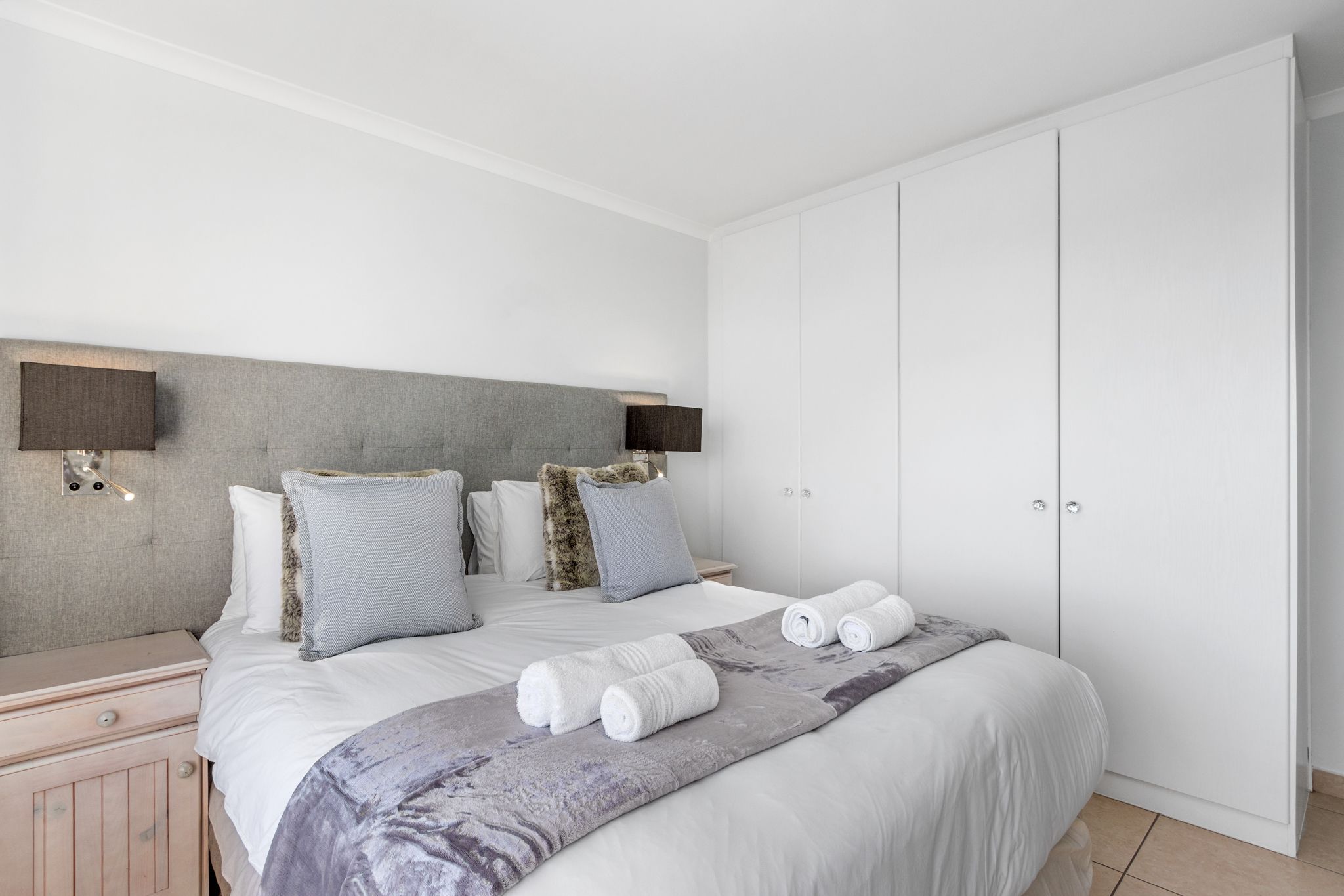 A bedroom with a bed, pillows, a blanket, a nightstand, and a wardrobe.
