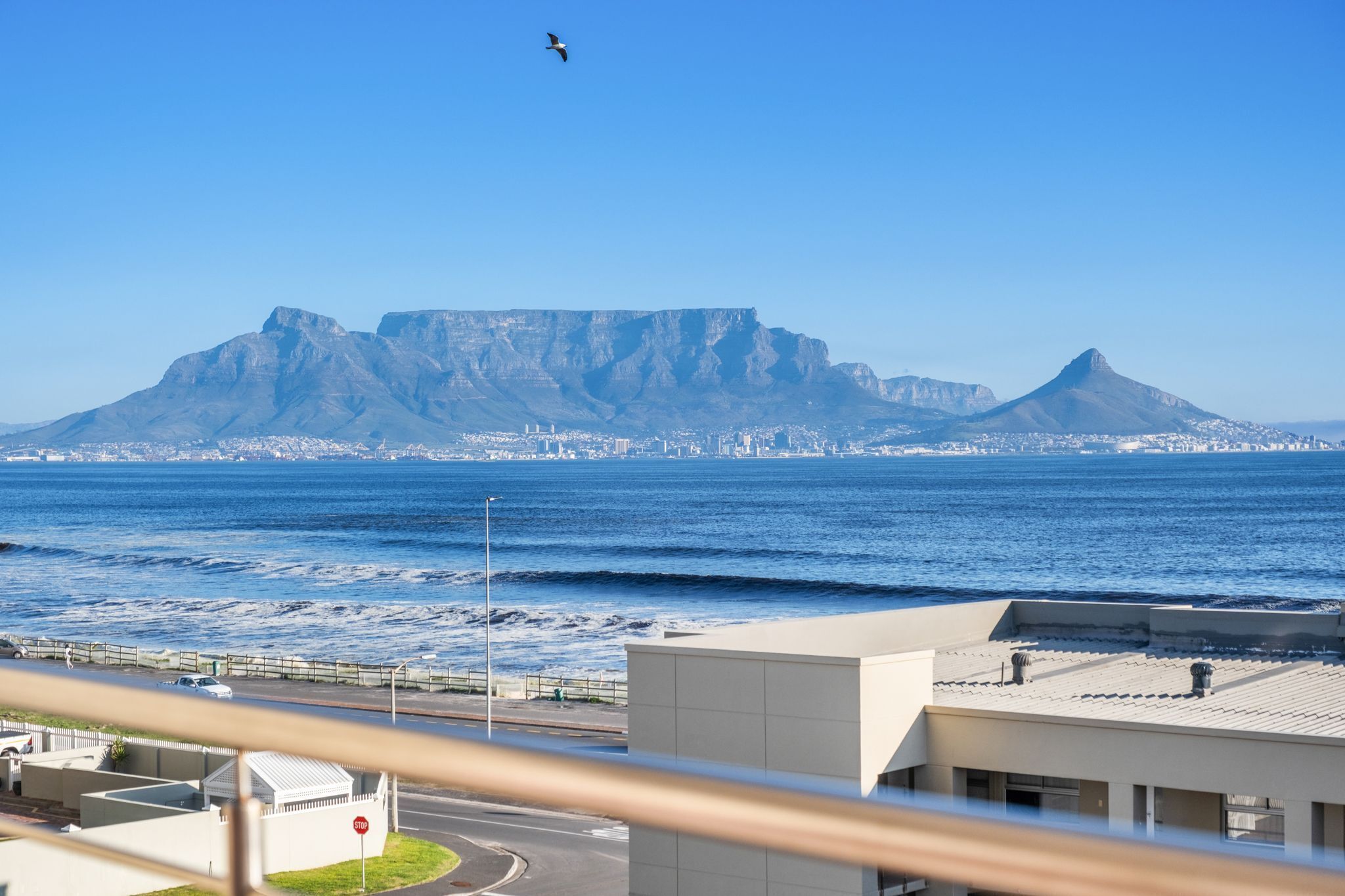 A coastal cityscape with a prominent mountain in the background, a view of the ocean, and a road with a stop sign.