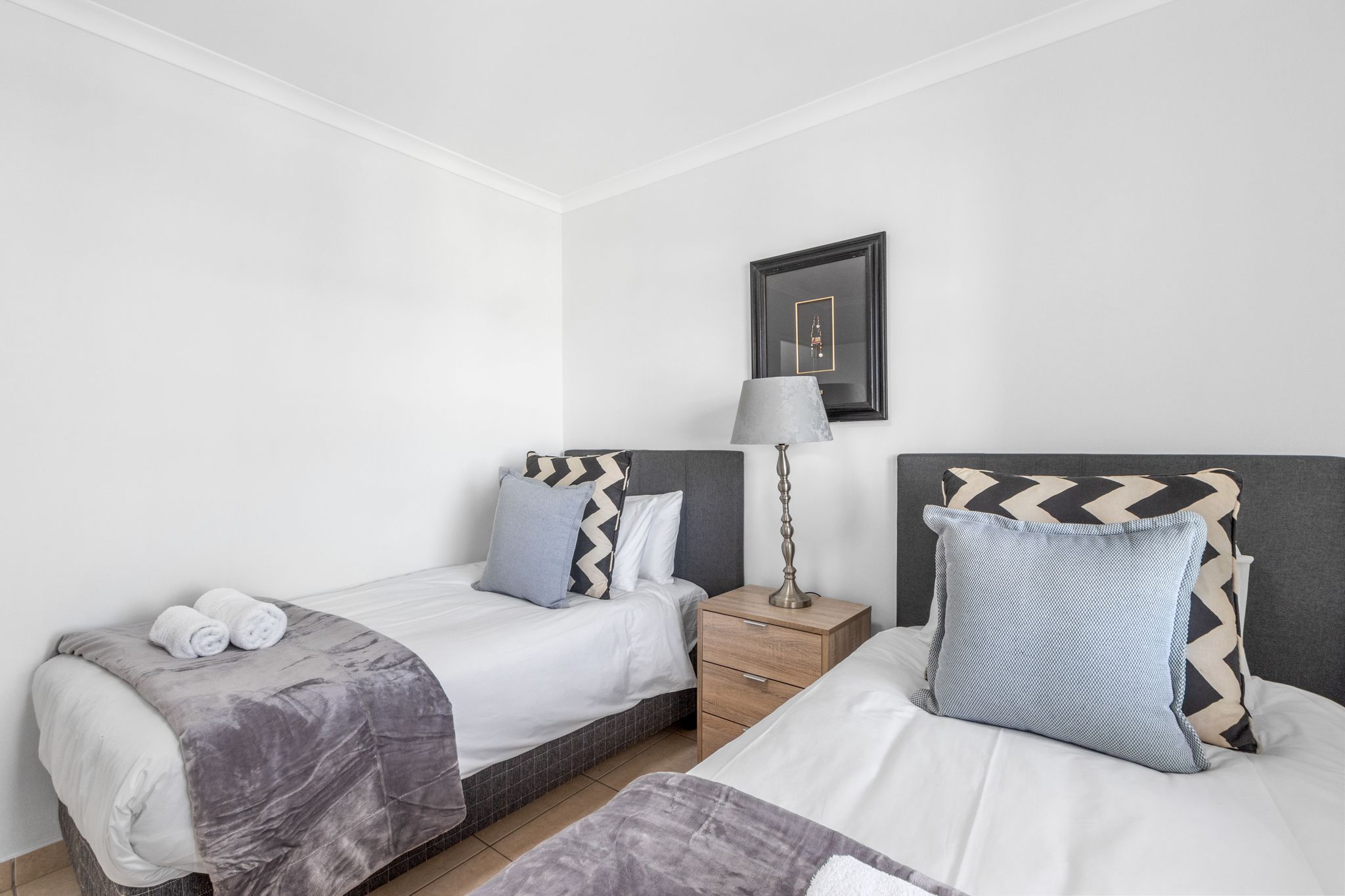 Ein Hotelzimmer mit zwei Betten, einem Nachttisch mit Lampe und einem gerahmten Bild an der Wand.