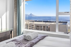 A hotel room with a large window offering a view of the ocean and a mountain. - The Waves 302 (Cape Town)