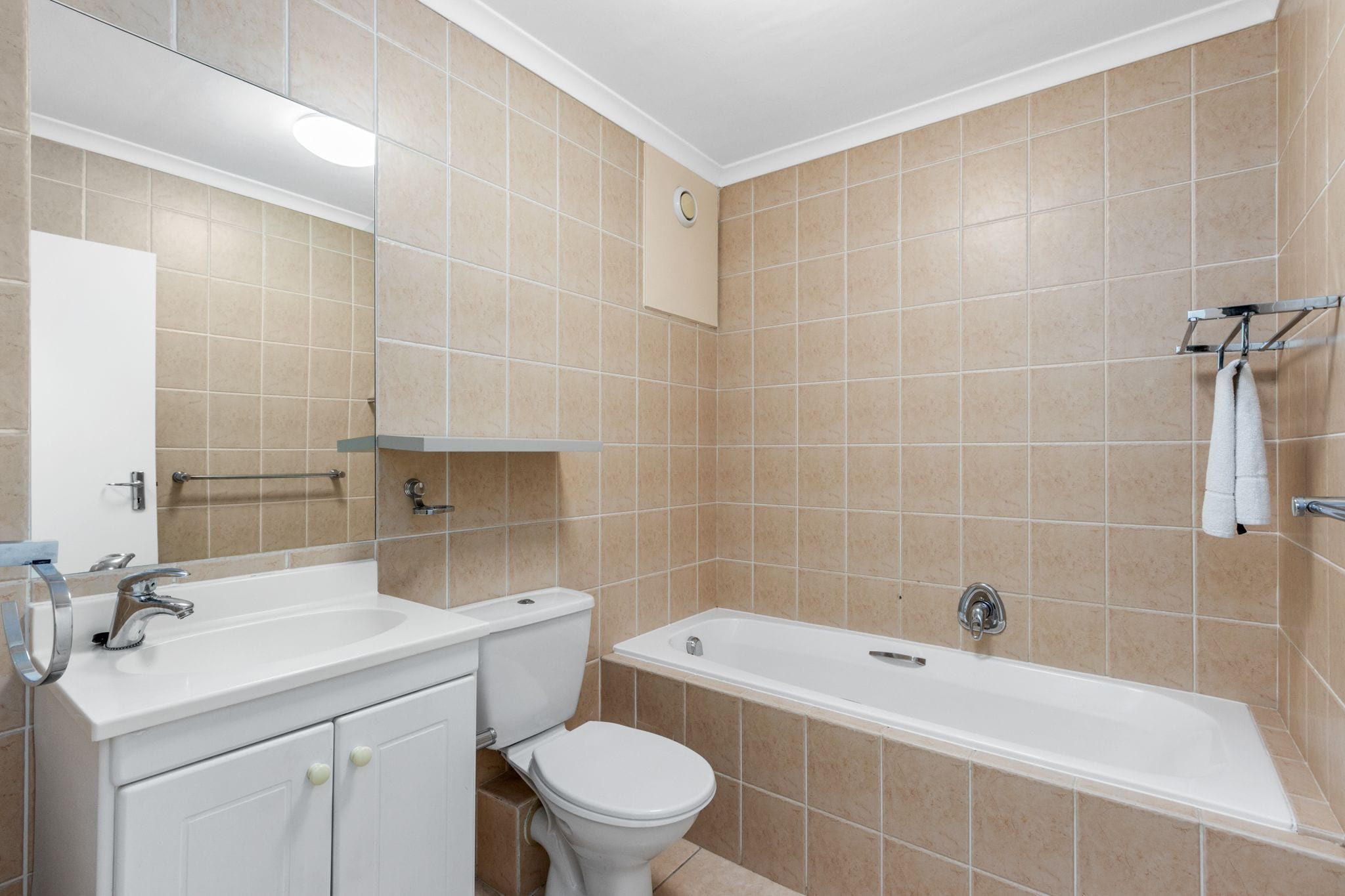 Une salle de bain avec des carreaux de couleur beige, un lavabo blanc, des toilettes et une baignoire.