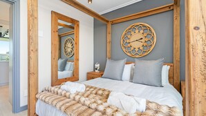 A bedroom with a wooden headboard, a large mirror, a decorative wall clock, and a bed with a patterned blanket and pillows. - Azul Terraces 101 (Cape Town)