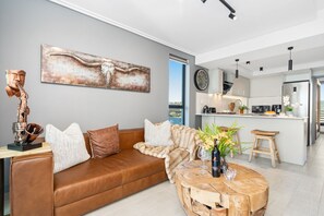 Un salon moderne avec un canapé en cuir marron, une table basse en bois et un grand tableau abstrait accroché au mur.