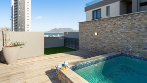 A rooftop pool with a stone wall and a view of a tall building in the background. - Azul Terraces 101 (Cape Town)
