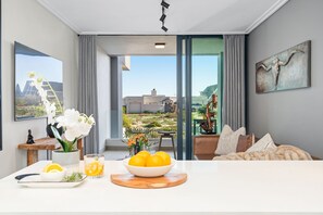 Un salon moderne doté d’une grande fenêtre, un coin repas avec une table dressée pour deux personnes, et une vue sur l’extérieur.