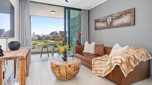 A modern living room with a brown leather sofa, a wooden coffee table, and a large window offering a view of the city. - Azul Terraces 101 (Cape Town)