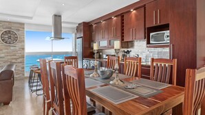 A modern kitchen with wooden cabinets, a stainless steel range hood, and a view of the ocean. - Silverwind - Blouberg Heights 1501 (Cape Town)