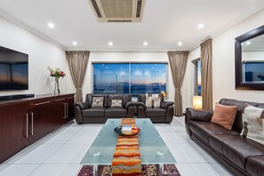 A modern living room with a sofa, a glass coffee table, a TV, and a view of the cityscape.