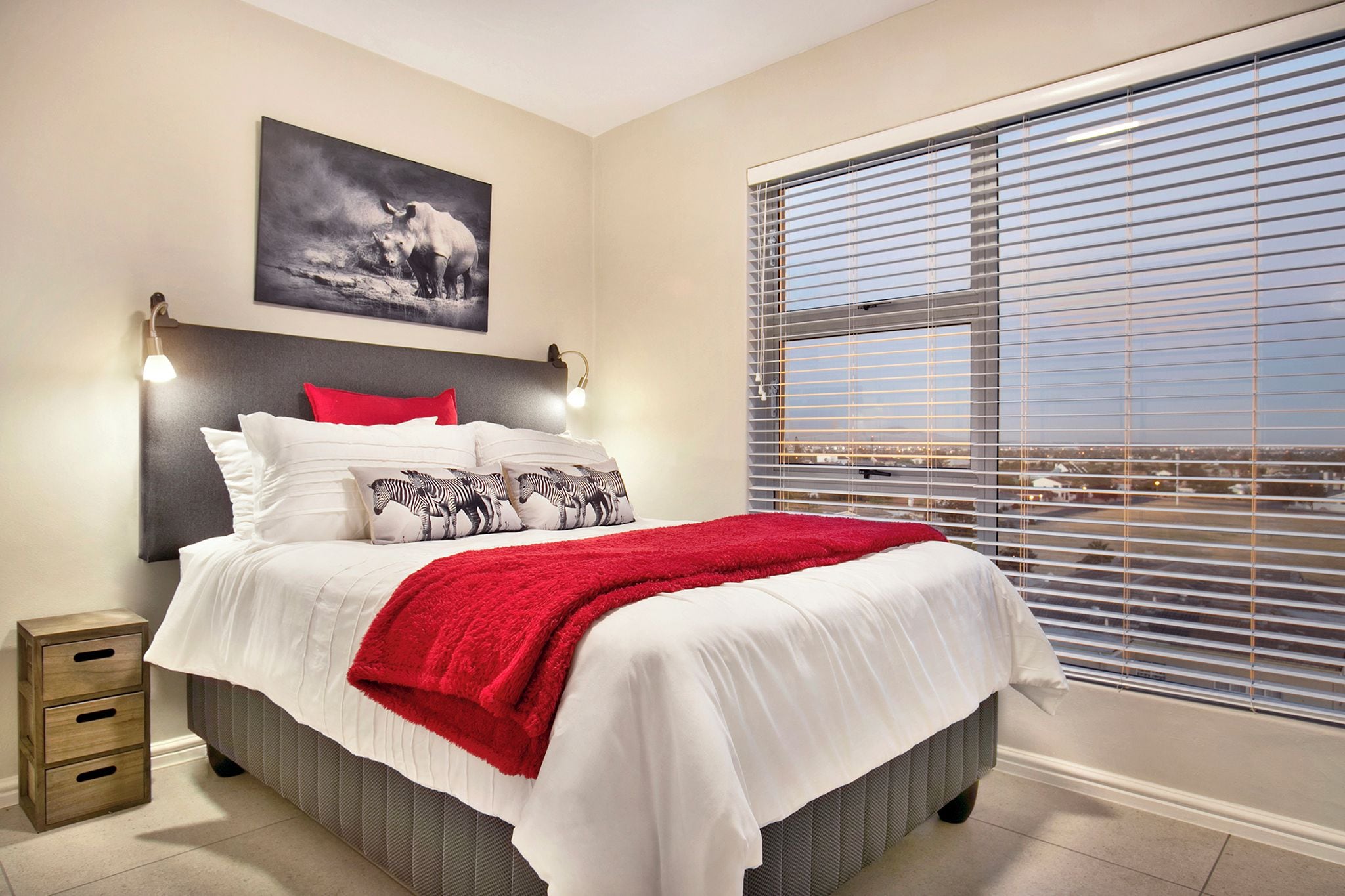 A bedroom with a bed, a nightstand, a window with blinds, and a wall-mounted picture.