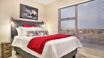 A bedroom with a bed, a nightstand, a window with blinds, and a wall-mounted picture.