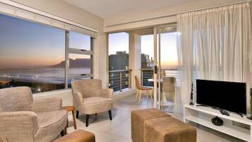 A spacious balcony with a view of the sea and cityscape, furnished with wicker chairs and a sofa.