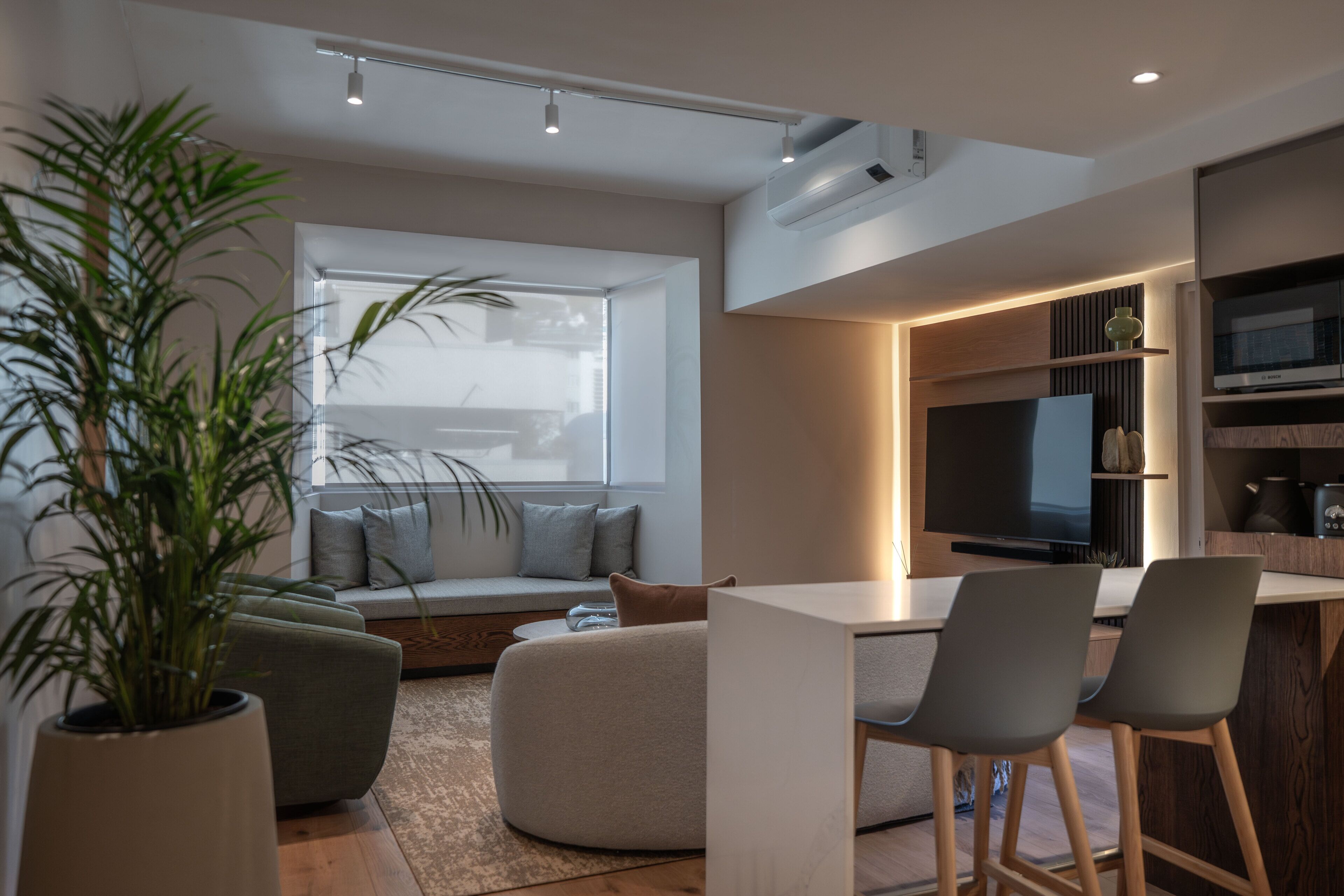 A modern living room with a sofa, a dining area with chairs, a large TV, and a potted plant.