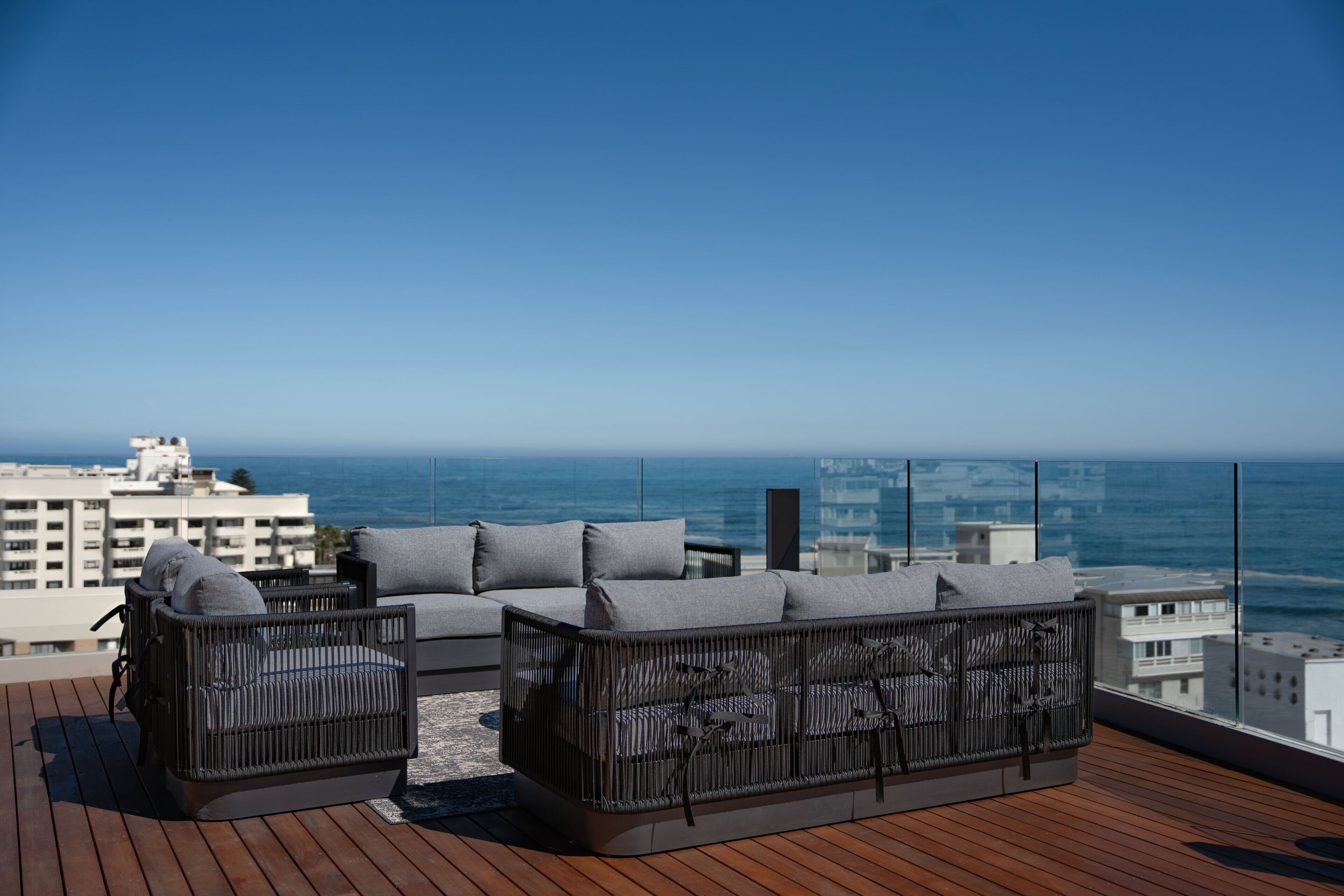 Un balcon agrémenté de meubles en osier, avec vue sur l’océan et des bâtiments en arrière-plan.