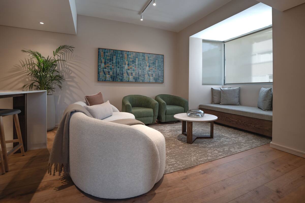 Un salon moderne avec un canapé, un fauteuil et des chaises vertes, une table basse, une grande fenêtre et un tableau accroché au mur.