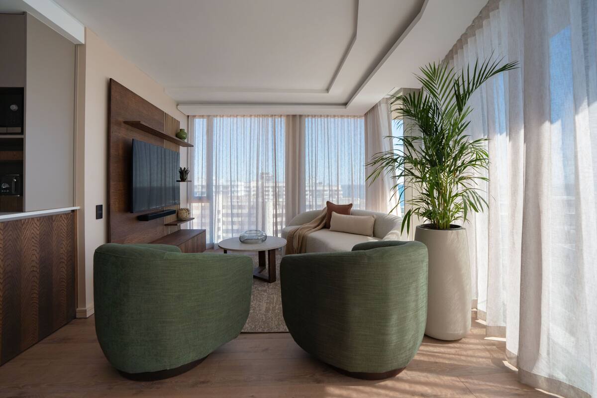 Un salon moderne avec un canapé, deux fauteuils, un téléviseur et une grande plante en pot.