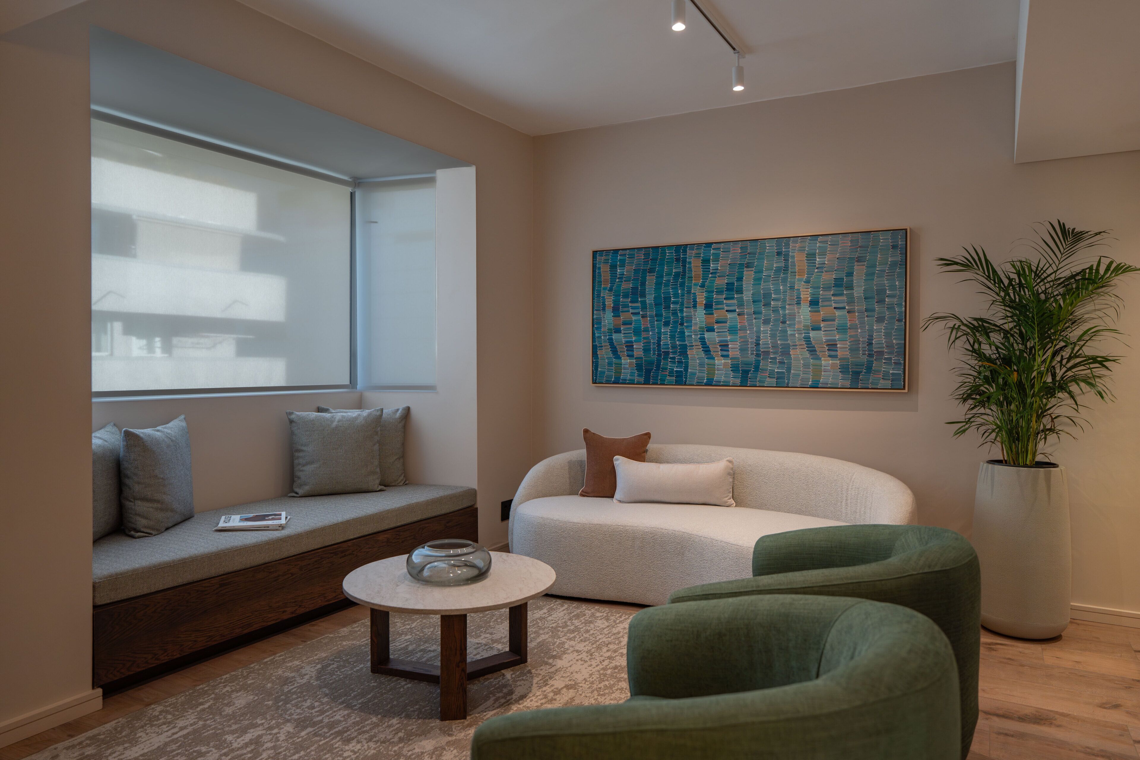 A modern living room with a sofa, a green armchair, a round coffee table, a large window, and a cityscape painting.