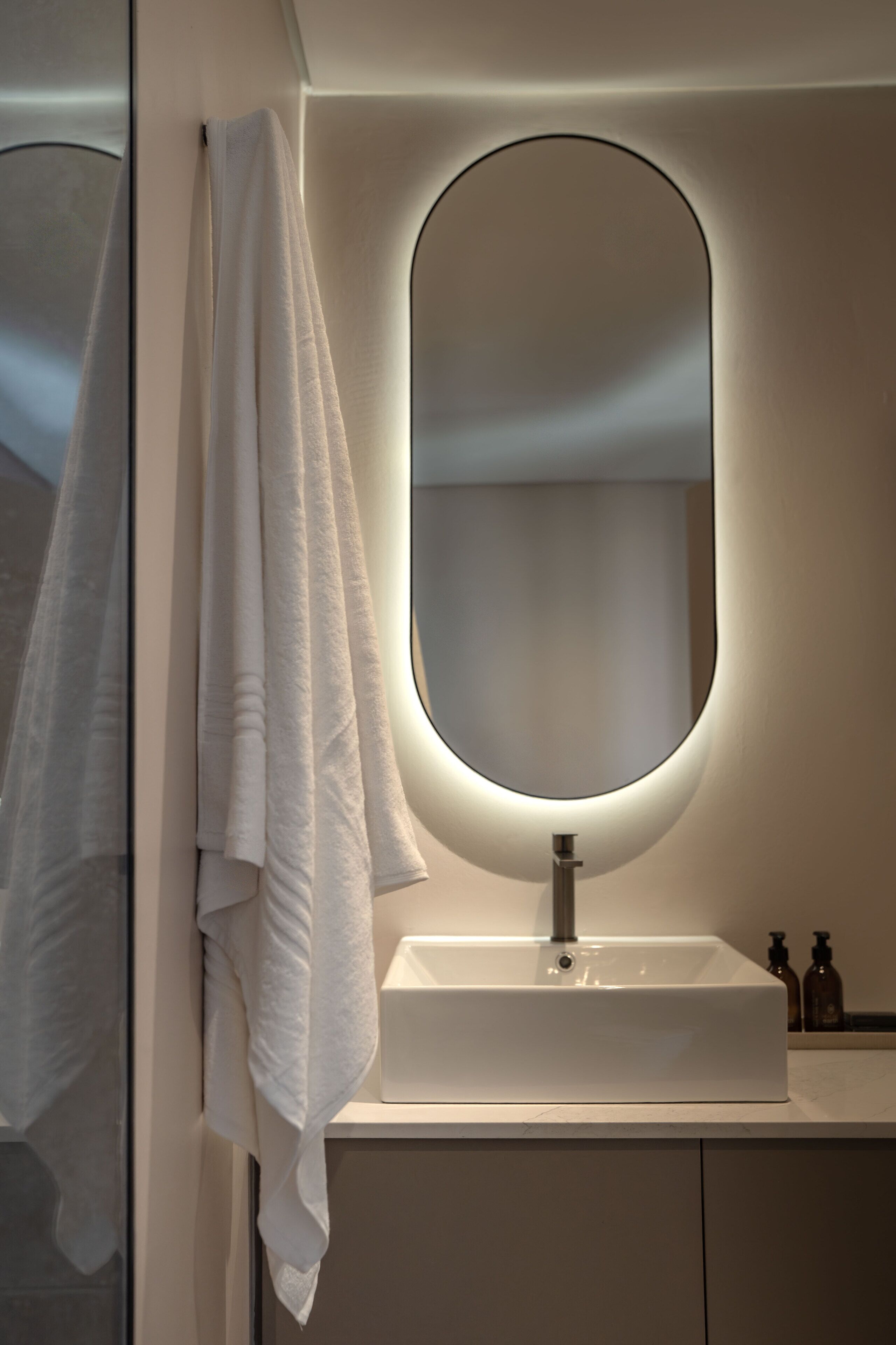 Een badkamer met een witte wastafel, een ronde spiegel en een handdoek aan de muur.