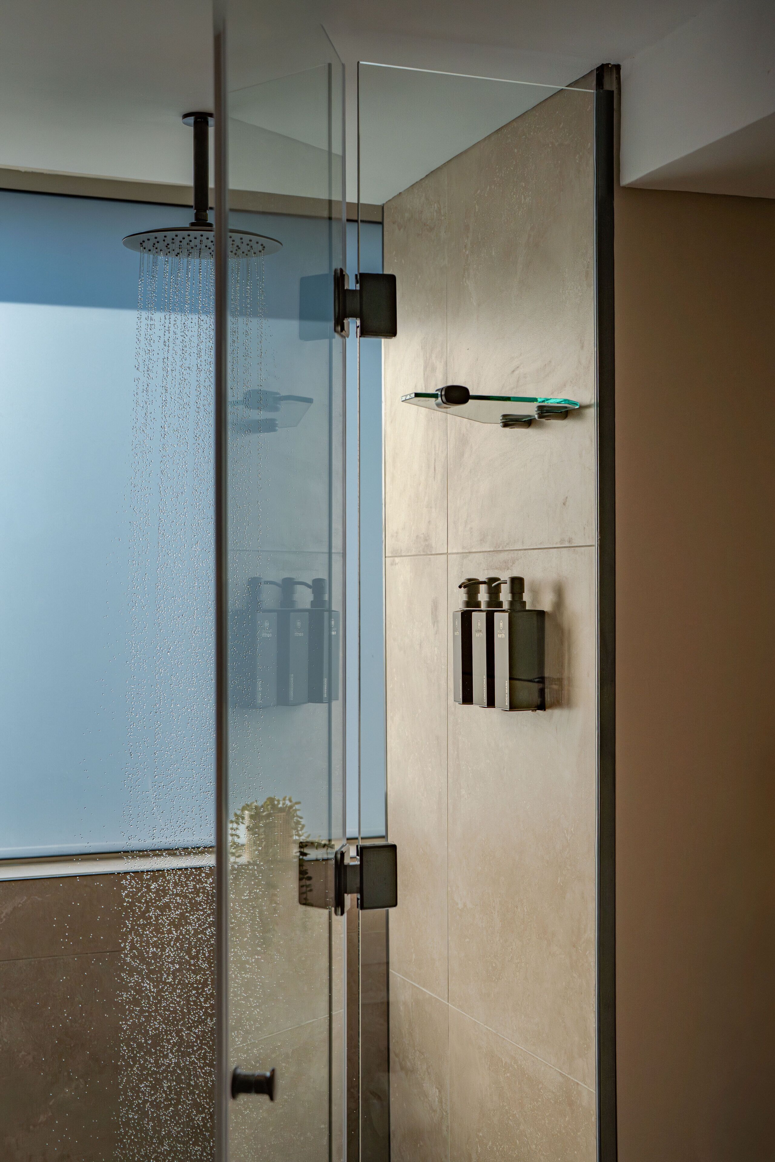 A modern shower with a rain showerhead, a glass door, and a wall-mounted faucet.